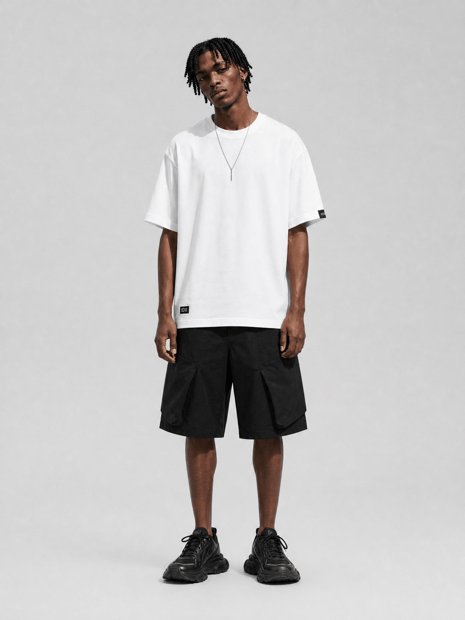 Person wearing a white t-shirt, black cargo shorts, and black sneakers on a gray background