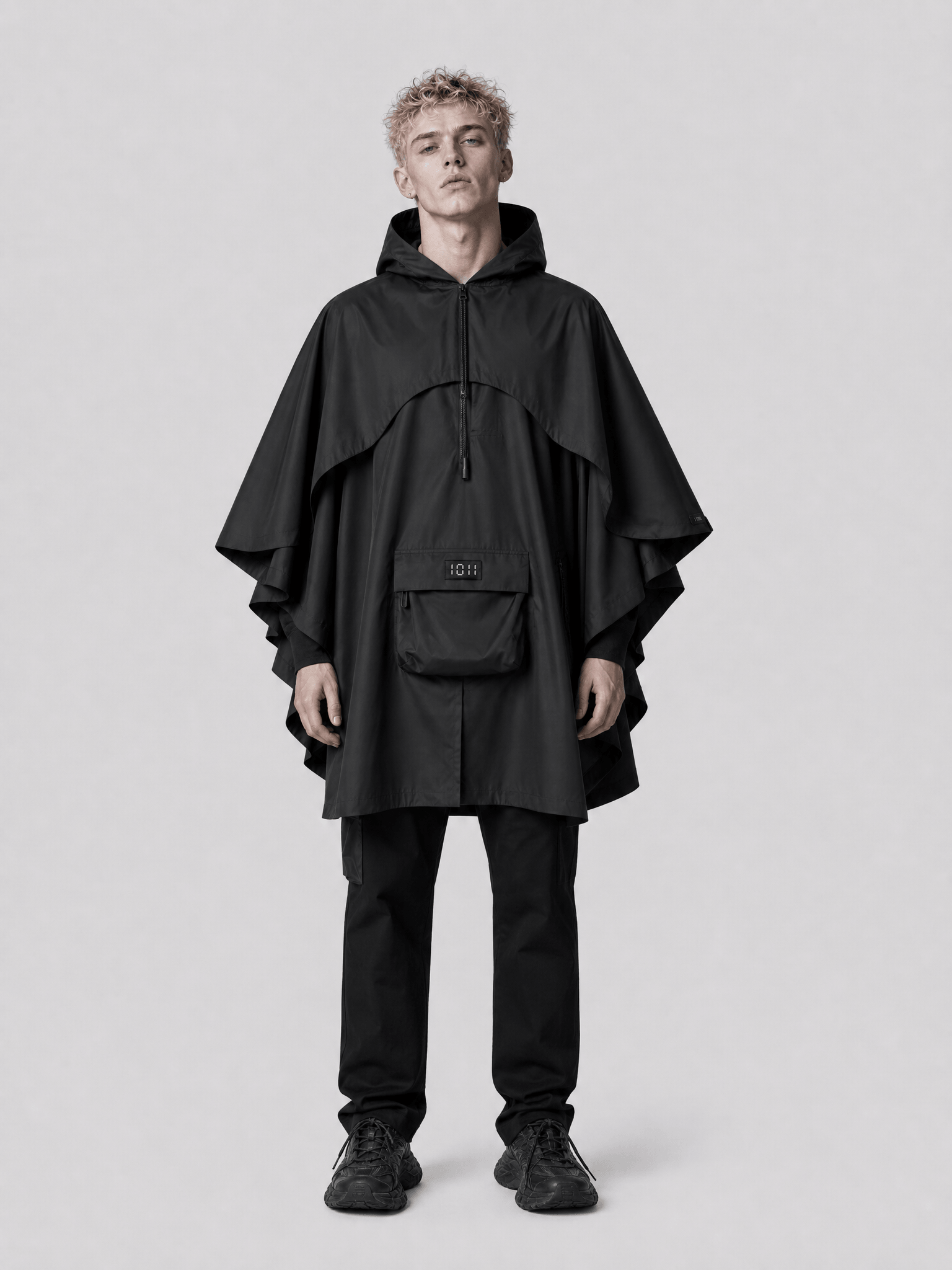 Person wearing a black poncho and pants on a light gray background