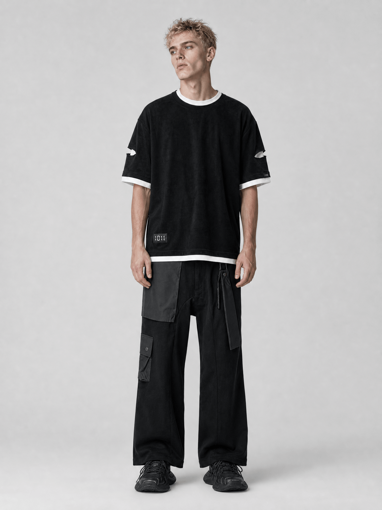 Person wearing a black oversized t-shirt and black cargo pants on a light gray background