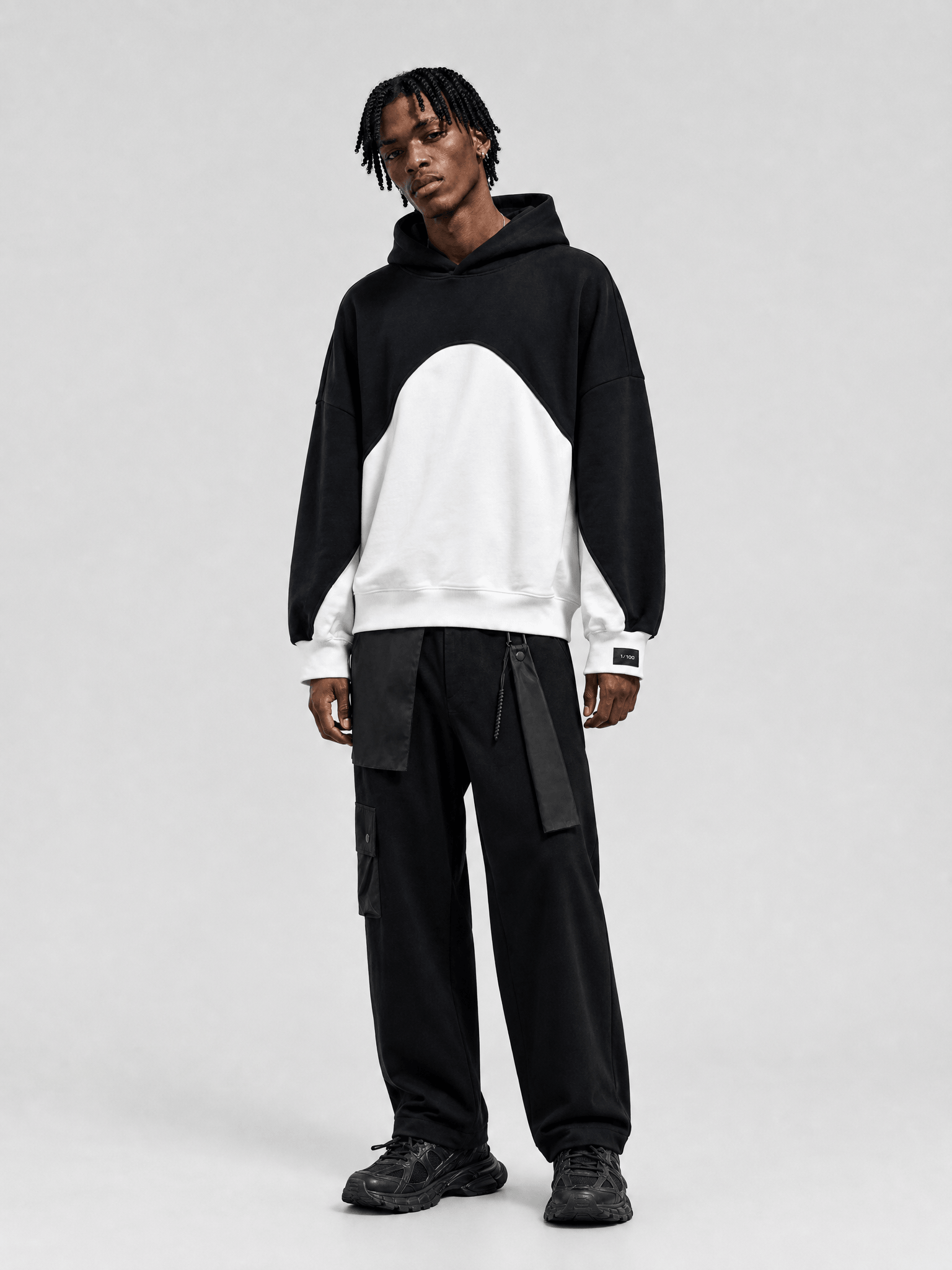 Person wearing a black and white color-blocked hoodie with black cargo pants on a white background