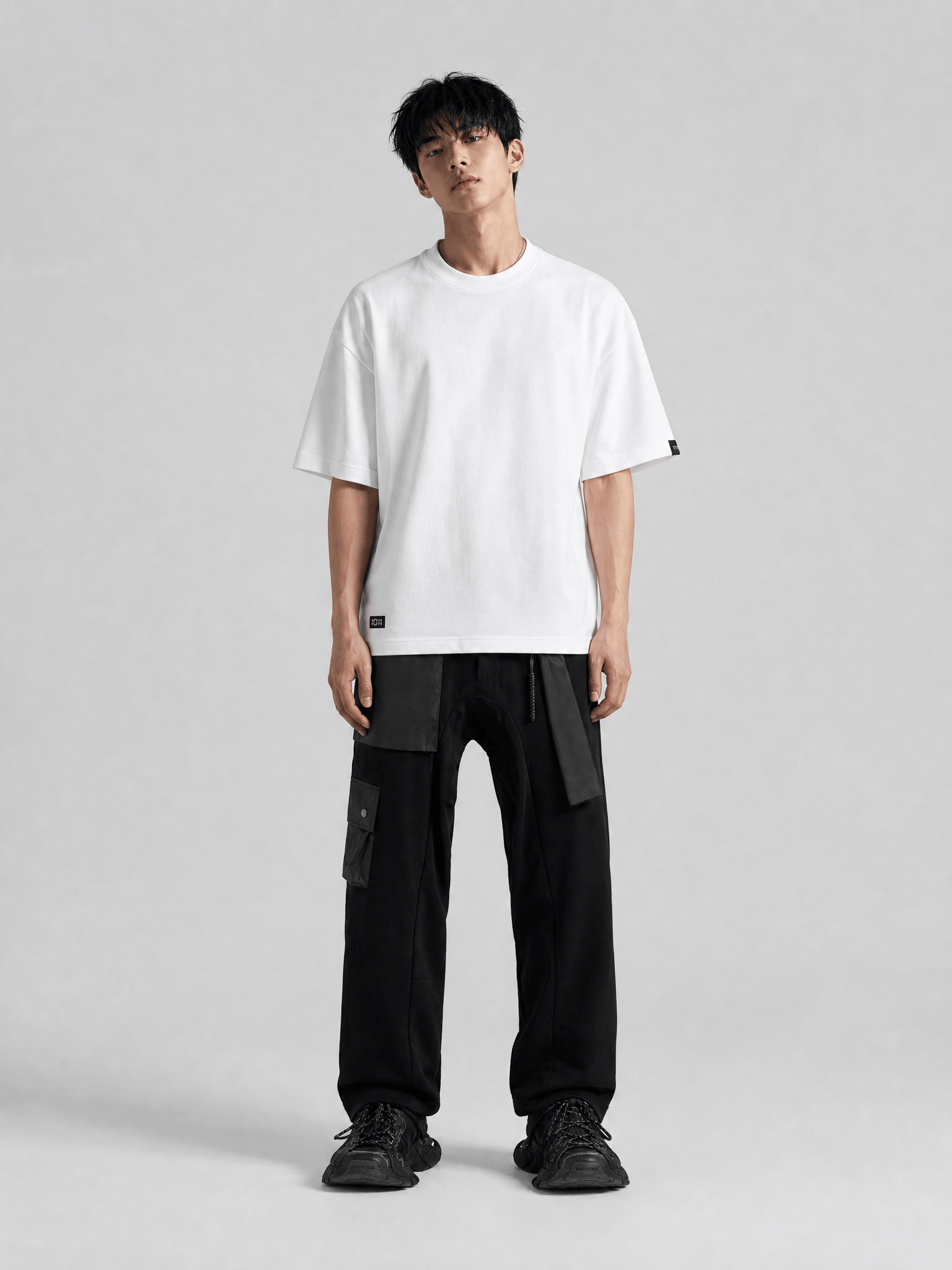 Person wearing a white t-shirt and black pants on a gray background